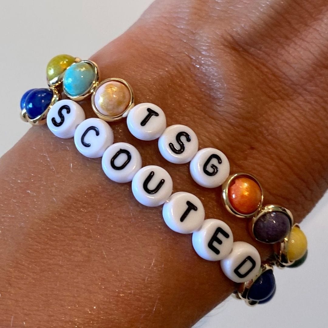 A colorful beaded bracelet with custom letters spelling "TSG SCOUTED," featuring vibrant gemstone beads in a casual, personalized style.