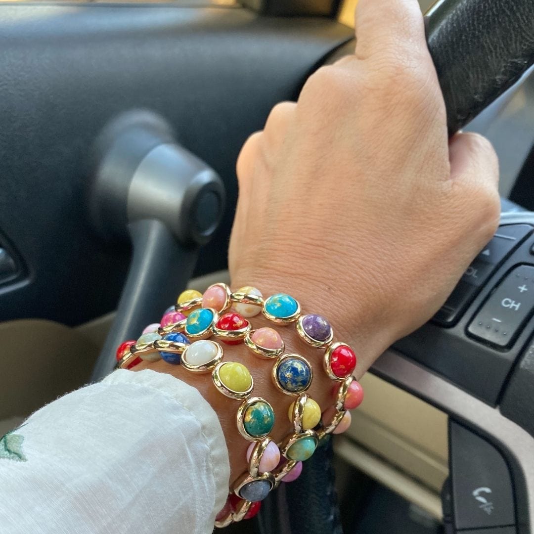 A close-up of a wrist wearing stacked colorful gemstone bracelets by Brett Lauren while holding a steering wheel.