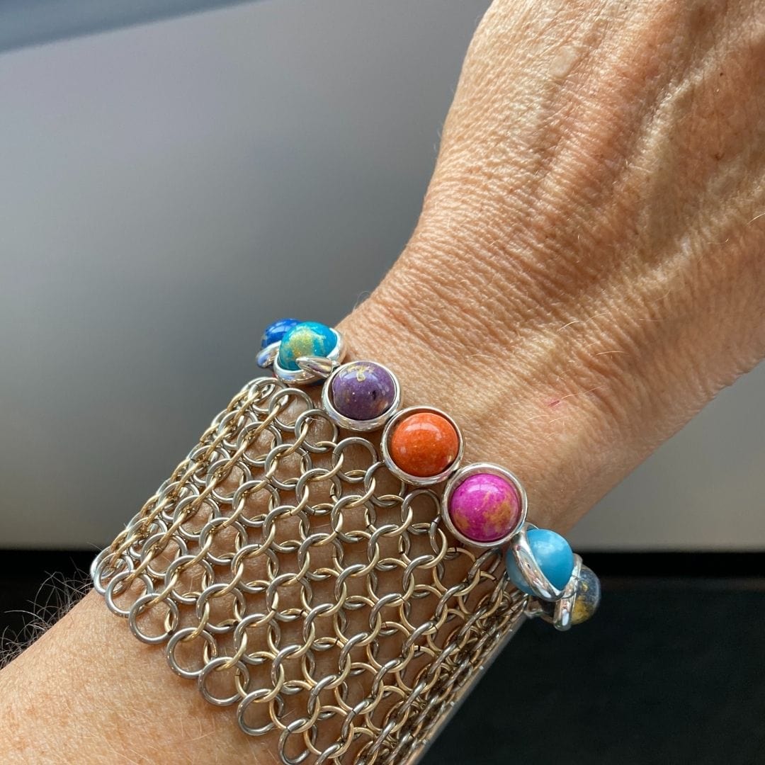 A close-up of a wrist wearing a gold bracelet with multi-colored beaded gemstones by Brett Lauren, displaying a vibrant and stylish design.