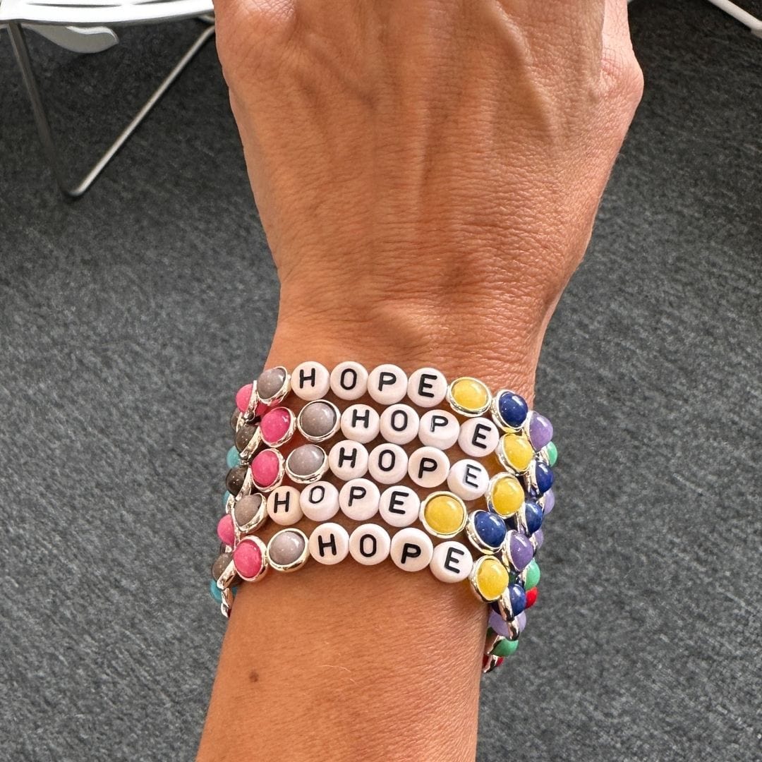 A wrist wearing stacked multi-colored gemstone bracelets by Brett Lauren, showcased in an outdoor setting.