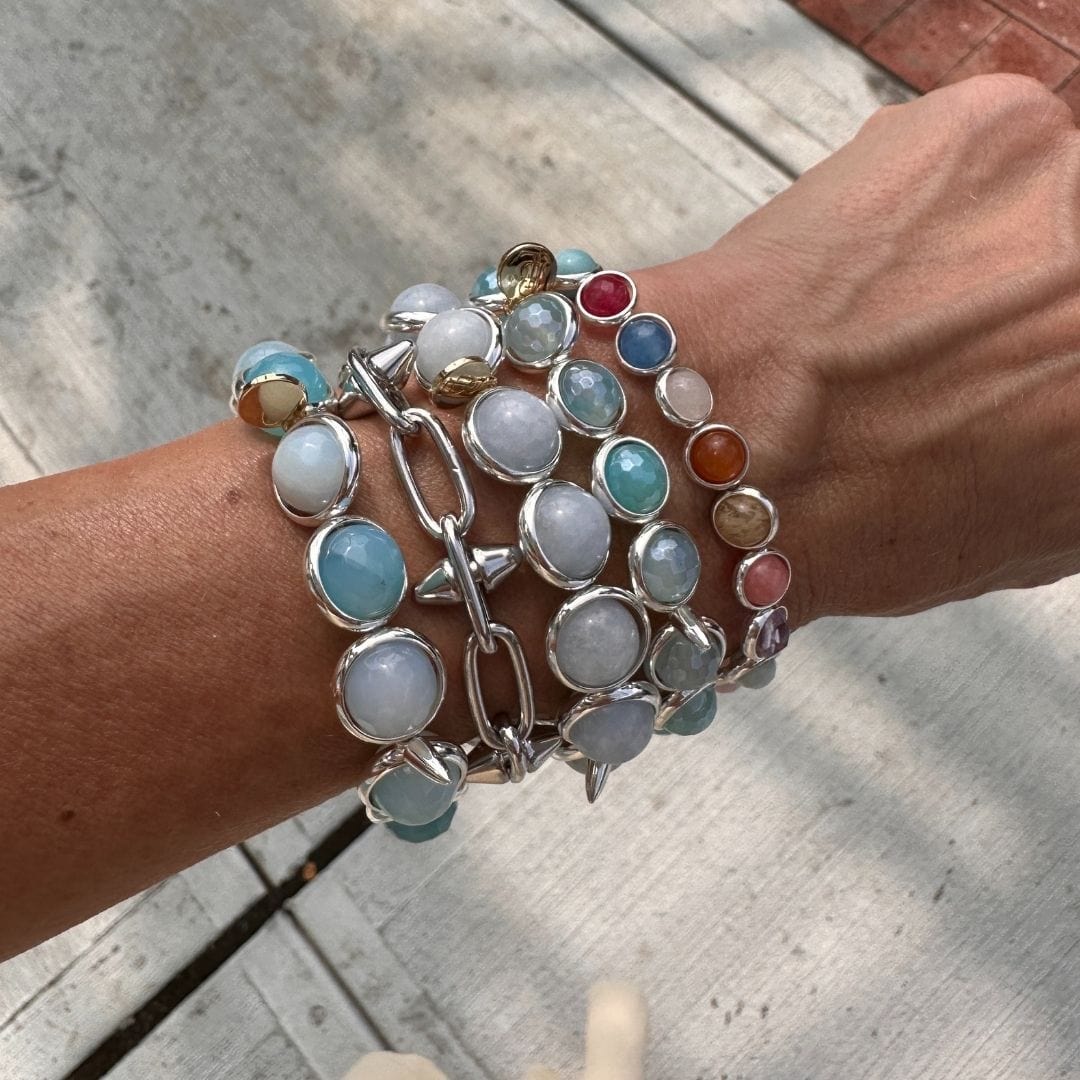 A close-up of a wrist adorned with multi-colored gemstone bracelets by Brett Lauren, styled outdoors with a mix of vibrant stones.