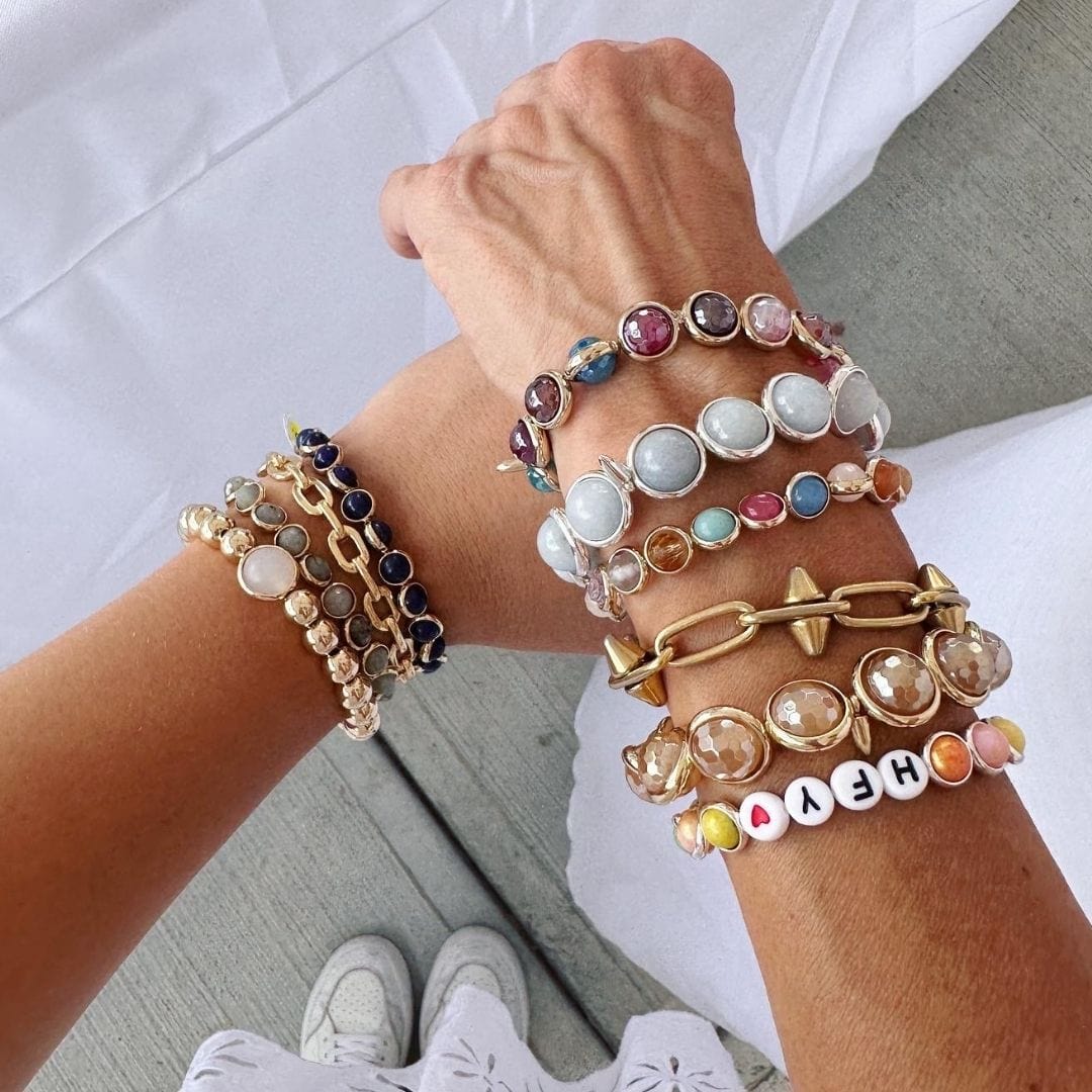 A close-up of a wrist adorned with stacked gemstone bracelets in various colors by Brett Lauren, paired with casual clothing.