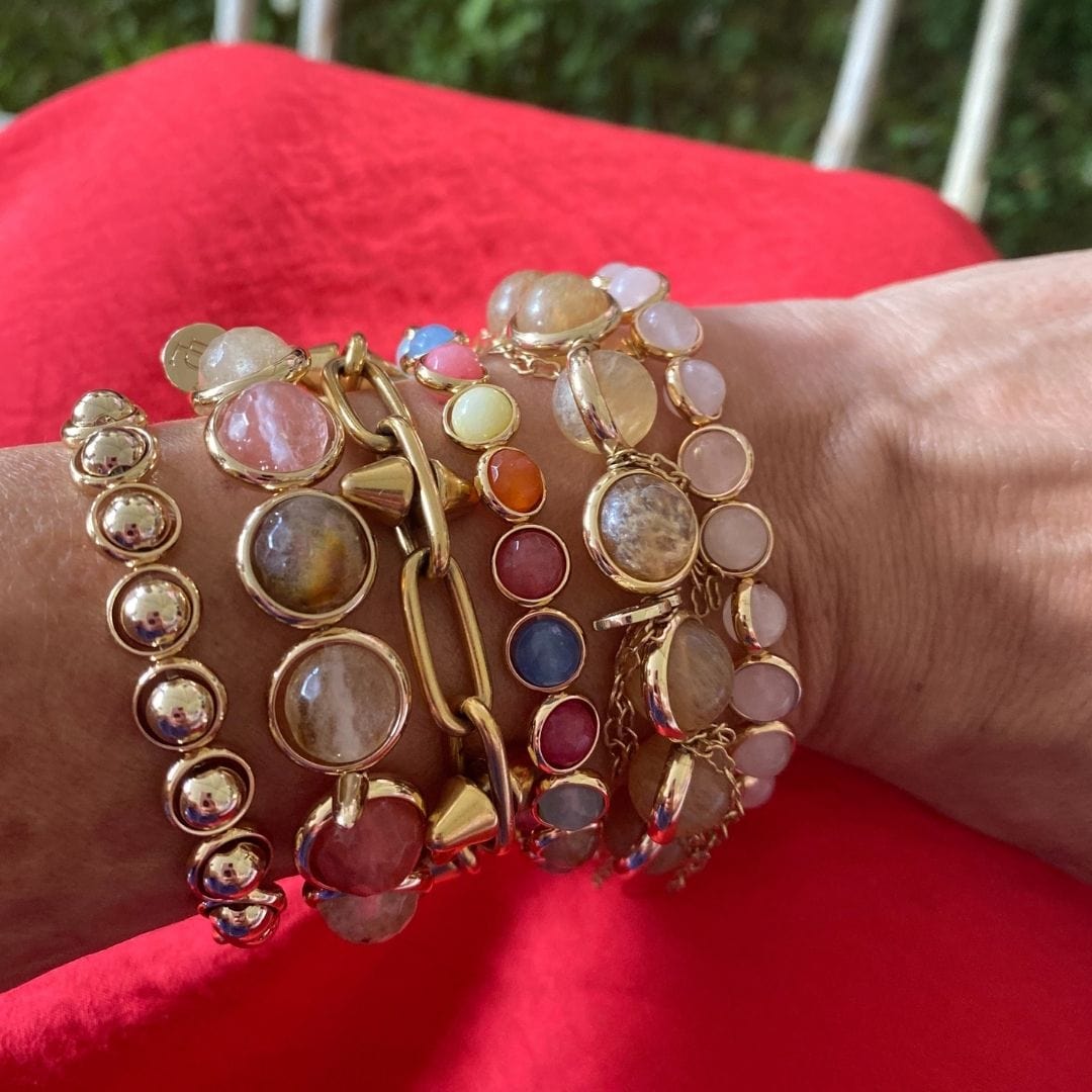 A woman wearing stacked gold and multi-colored gemstone bracelets by Brett Lauren, styled with a red dress.